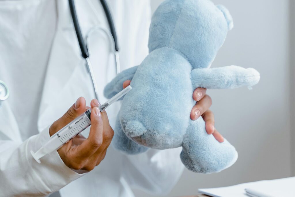 Close-up of a doctor using a syringe on a plush toy for educational purposes.